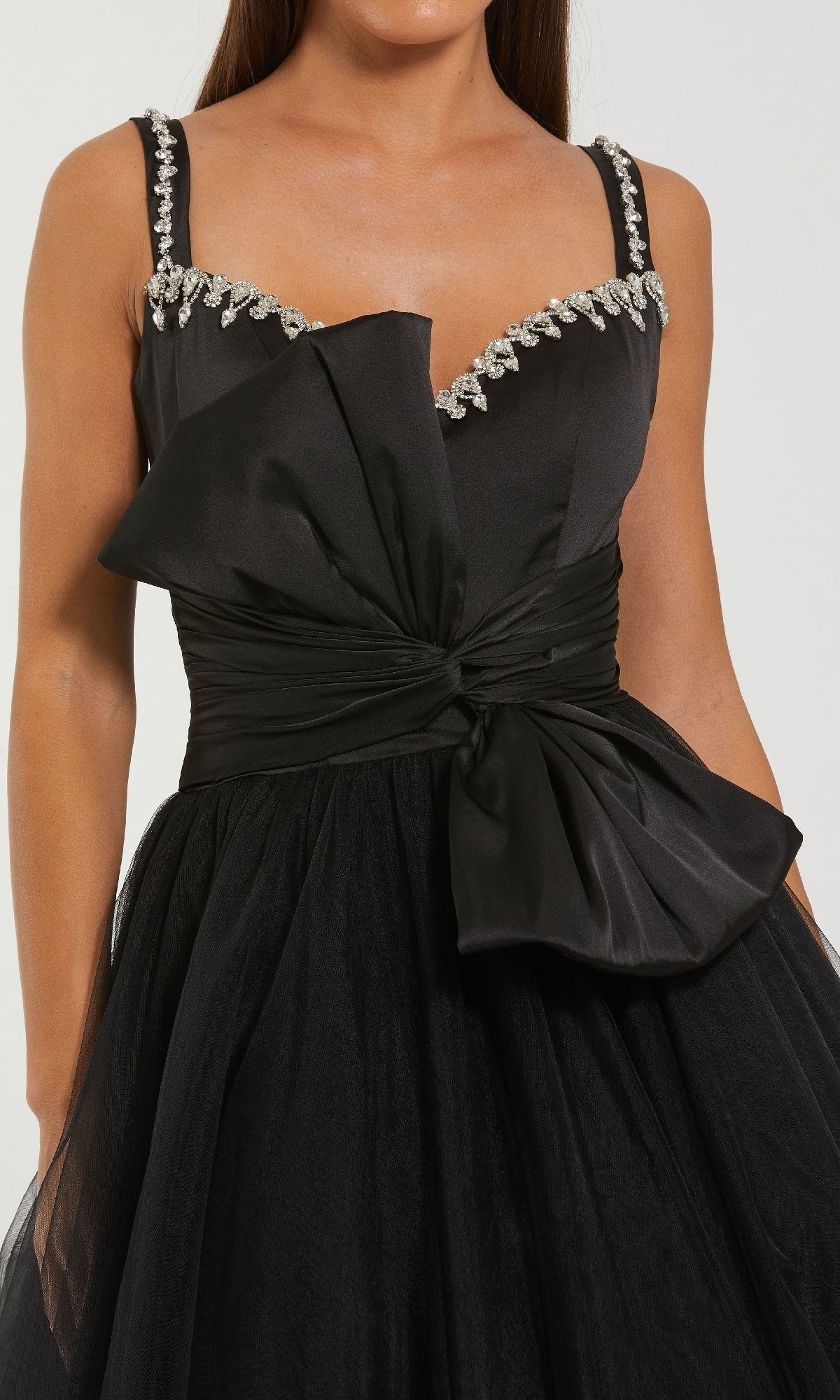 Close-up view of a bow detail on the front of a black ball gown a model is wearing with a white background.
